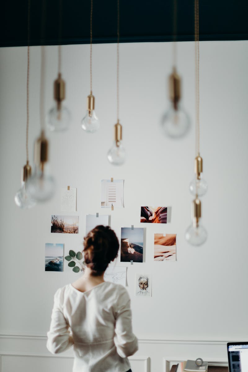 Woman in white top examining mood board under hanging lights in a modern interior design setting.